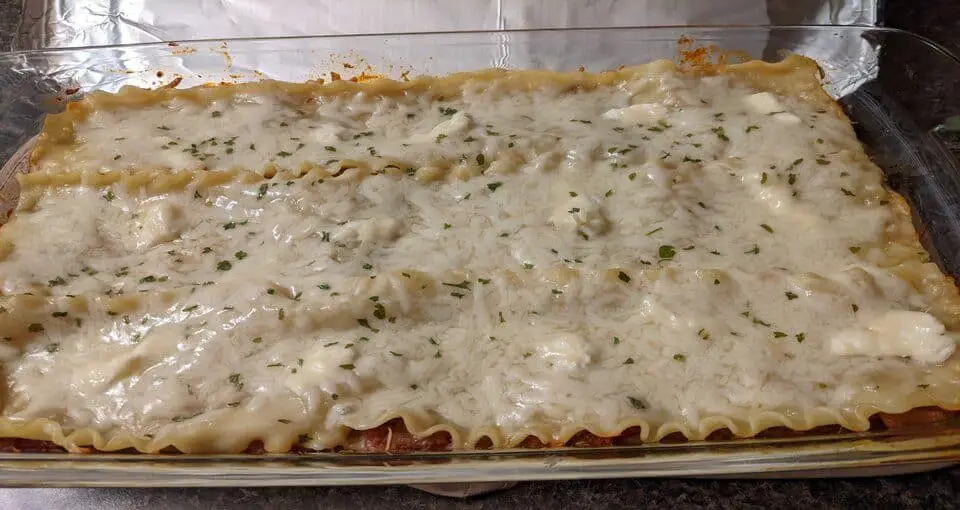 Aluminum foil sheet lifted off a baked lasagna in a glass pan.